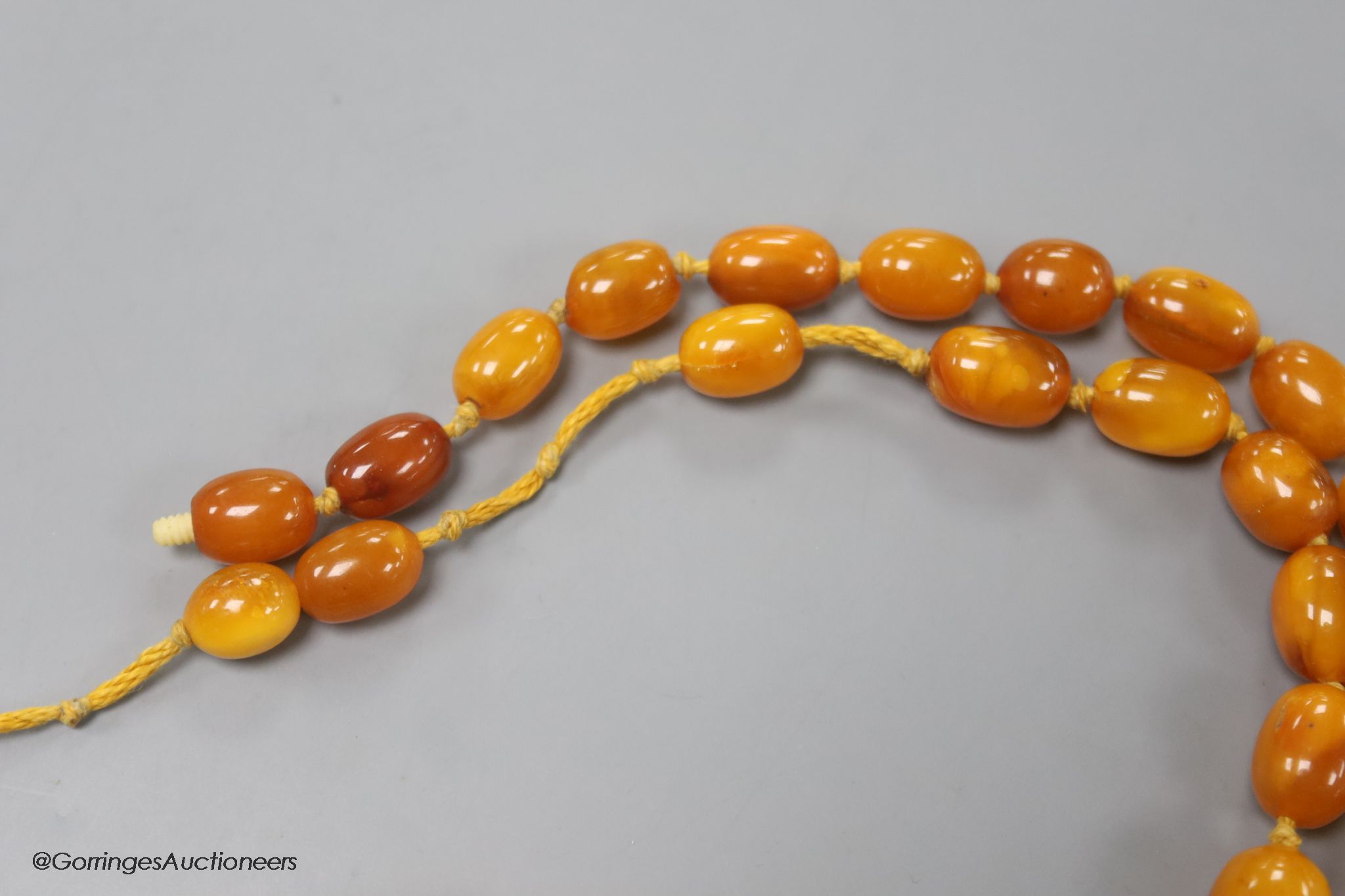 Two single strand graduated oval amber bead necklaces, 71cm, 61 grams & 89cm, 68 grams (beads missing from larger necklace)